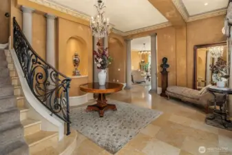 Step into Italian Renaissance-inspired interiors featuring Venetian plaster walls with ornate cornice moldings and Jerusalem gold marble floors throughout the main level. This grand entry showcases classical Roman columns, a sparkling crystal chandelier, and curved staircase with a custom wrought-iron railing featuring a Tuscan scrollwork design.