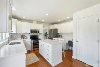 Bright, sparkling kitchen with quartz counters, stainless appliances, hardwood floors, island seating, built-in desk area, and pantry.