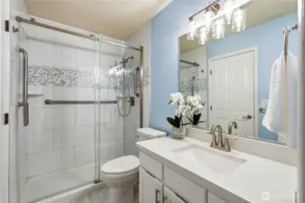 Updated main-level primary bath features a sleek step-in shower with custom tile detail, quartz countertop, modern lighting, and a spacious walk-in closet for added comfort and convenience.