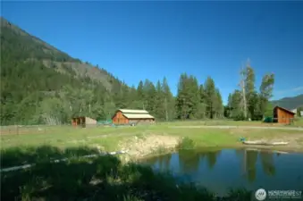 Peaceful pond framed by barn, forest, and mountains—wildlife haven and serene backdrop for ranch life