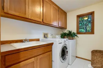 Well-appointed laundry room on the main floor with ample cabinetry, utility sink, and full-size washer and dryer that stay.