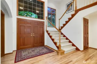 Step into a grand two-story foyer featuring elegant hardwood floors, a sweeping staircase, and striking double entry doors. Expansive windows fill the space with natural light, creating a warm and welcoming first impression.
