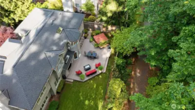 Aerial view reveals a beautifully maintained home with a spacious deck, lush lawn, and direct access to a scenic greenbelt trail. Surrounded by mature trees, this private outdoor oasis is ideal for peaceful living and effortless entertainment.