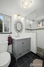 A handsome three-quarter primary bath boasts of custom tile and vintage look vanity.