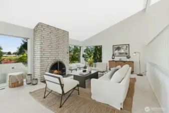 Light-filled living room with masonry fireplace, walls of windows & vaulted ceilings