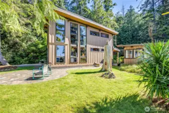 Side of the home with small patio, grassy area and out building beyond. Beautiful light here.