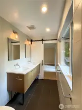 The clean lines of the primary bath amplify its sense of luxury and space featuring  tile all around, a floating style double vanity, spacious walk-in shower and expansive glass that frames a private backyard view.
