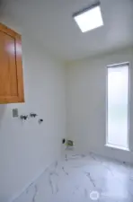 Utility room has tile flooring, floor to ceiling frosted glass window, and cabinet.