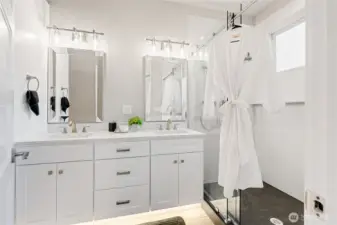 The downstairs primary bathroom features a double sink vanity, under cabinet lighting, solid one piece quartz shower, with a solid one piece quartz pan! This is a very rare feature, making the shower a seamless beauty that is easy to clean and maintain! You also have a tall linen cabinet to the left.