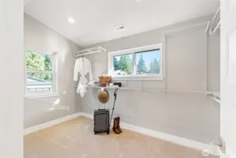 Huge walk-in closet with two windows and built-in shelving and hangers.