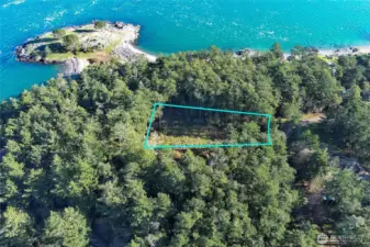 Aerial view of the level, partially cleared .48-acre lot in Cape San Juan with property lines shown, surrounded by mature evergreens and located near the shoreline on San Juan Island.
