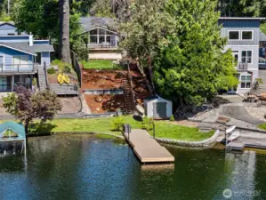 From the Dock to the Deck, Lakeside Living Done Right. This aerial view showcases it all—your own private dock, lush lawn, kayak storage, and a staircase leading up past terraced landscaping to a home that’s all about easy living. And with well-maintained neighbors, the community vibe here is just as welcoming as the view.