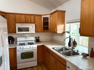 This light-filled galley kitchen features generous counter space, a charming greenhouse window over the sink, and garden views that make meal prep a pleasure. The stove anchors the end of the kitchen with work zones on both sides for efficiency.