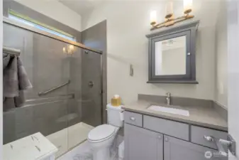 En-suite guest bath with Quartz counters, tile shower surround, tile flooring and a custom framed mirror/medicine cabinet.