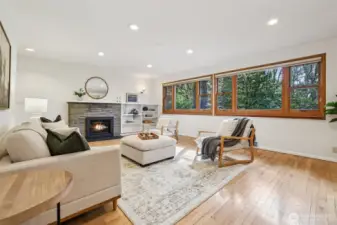 Spacious  living room features gas fireplace & wall of windows with serene forest  views.