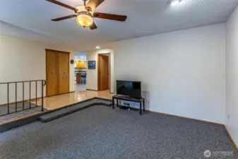 The living room, features a ceiling fan and a wood burning stove. The kitchen is straight ahead.