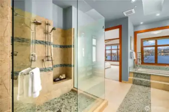 A space that feels like a spa—walk-in glass shower with pebble underfoot, layered tile, and a seamless connection back to the suite.