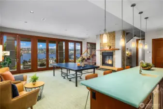 Expansive lower-level entertainment area featuring a stone fireplace, wet bar with quartz countertop, and full-height glass doors opening to the waterfront patio. Enjoy lake and mountain views from this versatile space, perfect for game nights and gatherings.