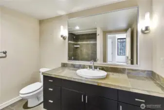The bathroom features a tiled shower-tub combination with earthy stone finishes, complementing the vanity design