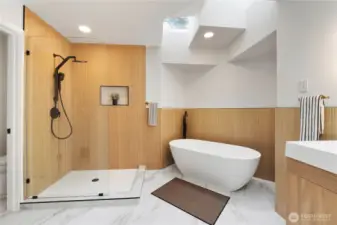 A stunning, spa-inspired bathroom showcasing a sleek glass-enclosed walk-in shower, matte black fixtures, and a sculptural freestanding tub. Warm tile paneling and a skylight create a bright, serene atmosphere