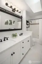 The updated upper level bathroom features dual sinks, a quartz countertop, tile flooring and a shower/tub with tile surround.