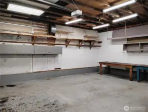 Plenty of lighting in this garage which has a automatic door opener, permanent mounted shelves and several movable workbench tables.