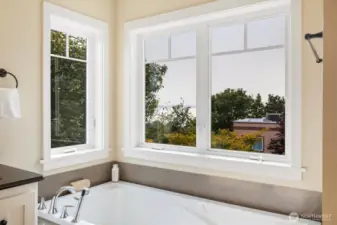 The spa-inspired primary bath features dual vanities, a soaking tub framed by windows, and a walk-in glass shower. Thoughtful finishes and natural light create a serene retreat for daily routines or unwinding at the end of the day.