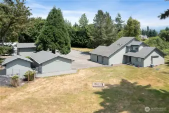 This picture shows front entry to home plus stand alone three car garage with extra workspace, smaller fully enclosed storage building for storage of grounds maintenance equipment, and fully enclosed high ceiling storage building.