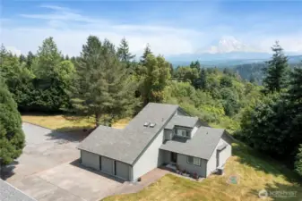 Aerial view of home facing south east with unobstructed view of Mt. Rainier.  Note large paved parking area between home and free standing three car garage.
