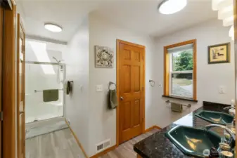 Primary 3/4 bathroom.  Double sink vanity.  Skylights bring in ample ambient light. Door opens into a large walk in closet, and then into a very large walk in attic storage area.