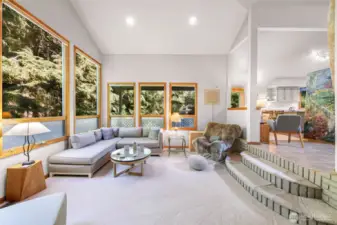A wall of windows frames the lush greenbelt, filling the living room with light and offering a serene connection to nature.