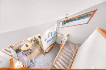 From the loft, the dramatic entryway and angular architectural details make a stunning impression, complemented by expansive tile flooring and vibrant natural light from the geometric upper window.