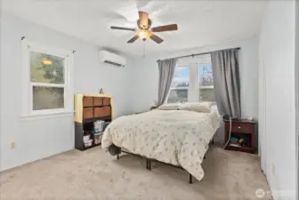 The main-floor primary bedroom is bright and spcious with soft carpeting, large windows and ceiling fan.