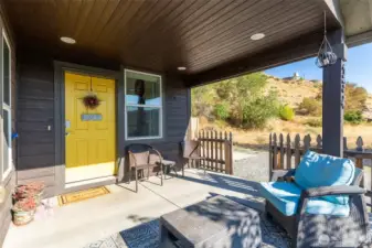 Welcoming covered porch with a sunny yellow door and plenty of space to relax outdoors.