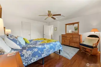 Fully furnished upstairs bedroom with a comfortable bed, dresser, ceiling fan, and cozy rocking chair.