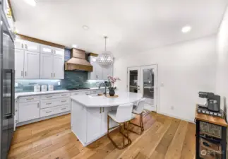 The gourmet kitchen boasts pristine white cabinetry, quartz countertops, and a central island with seating. Highlighted by a designer pendant light, this kitchen blends function and style.