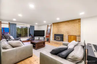 The spacious living room features hardwood floors, a cozy fireplace with a brick surround, and large windows that let in natural light. A welcoming space for relaxation or hosting guests.