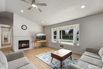 Living room featuring wood-burning fireplace, large front-facing windows, recessed lighting, ceiling fan, and updated flooring.