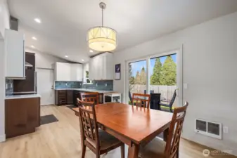 Open dining area flowing into remodeled kitchen with quartz countertops, two-tone cabinetry, blue tile backsplash, and sliding glass door to fully fenced backyard.