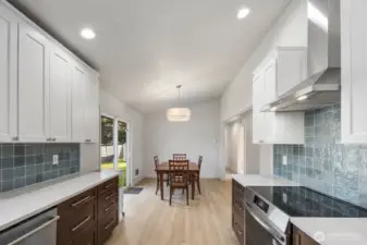 Remodeled kitchen with quartz countertops, induction range, stainless vent hood, two-tone cabinetry, blue tile backsplash, and open view to dining area with sliding glass door.