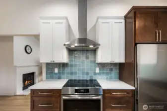 Induction range with stainless steel vent hood and modern tile backsplash.
