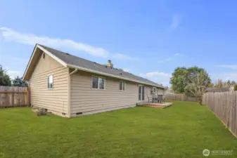 Rear exterior highlights easy indoor-outdoor access from the sliding glass door to the patio, opening to a broad, level backyard enclosed with wood fencing
