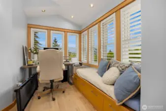 A sweet home office space occupies the corner of the primary bedroom with built-in desk and cozy window bench seating. Try getting work done with the big windows and view!