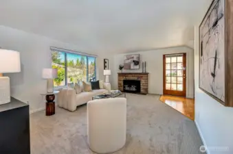 One of two living areas, the main-floor living room featuring a beautiful MCM stone surround wood-burning fireplace and large windows. This versatile floor plan offers two separate areas for everyone to spread out and enjoy. New carpet and paint throughout!