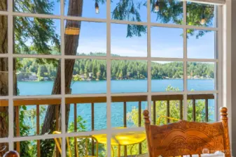Lake view from inside the cabin through large grid window framed by trees and deck railing.