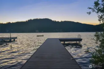 Dock at sunset with calm water and hills silhouetted across the lake.