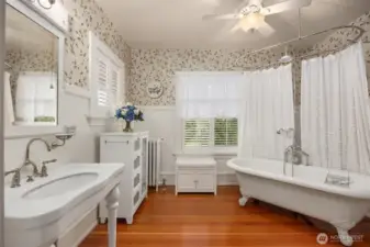 A spa-like main hall bath blends vintage elegance with thoughtful updates. A classic clawfoot soaking tub and shower with a separate walk-in shower, pedestal sink, patterned wallpaper, and original details create a serene retreat that feels both timeless and indulgent.