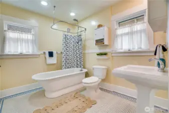 The upstairs bathroom boasts original penny tile, a classic chair rail, two bright windows that let in plenty of natural light, a modern pedestal sink, and extra medicine cabinets.