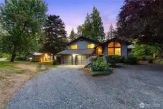 Twilight shot capturing the main home and versatile outbuilding, both glowing with light—an Arlington property that blends comfort, function, and privacy.