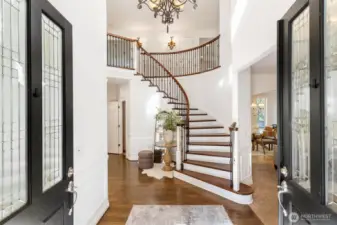 Elegant entryway showcasing a dramatic curved staircase with dark wood treads and a classic chandelier.
